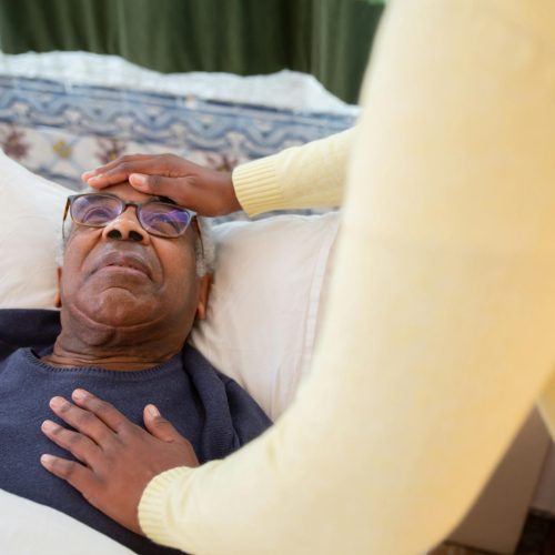 A caregiver attending to an elderly man in bed, providing comfort and support.